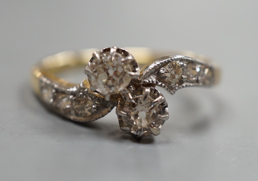 A yellow metal and two stone diamond set crossover ring, with diamond set shoulders, size J, gross weight 3.1 grams.